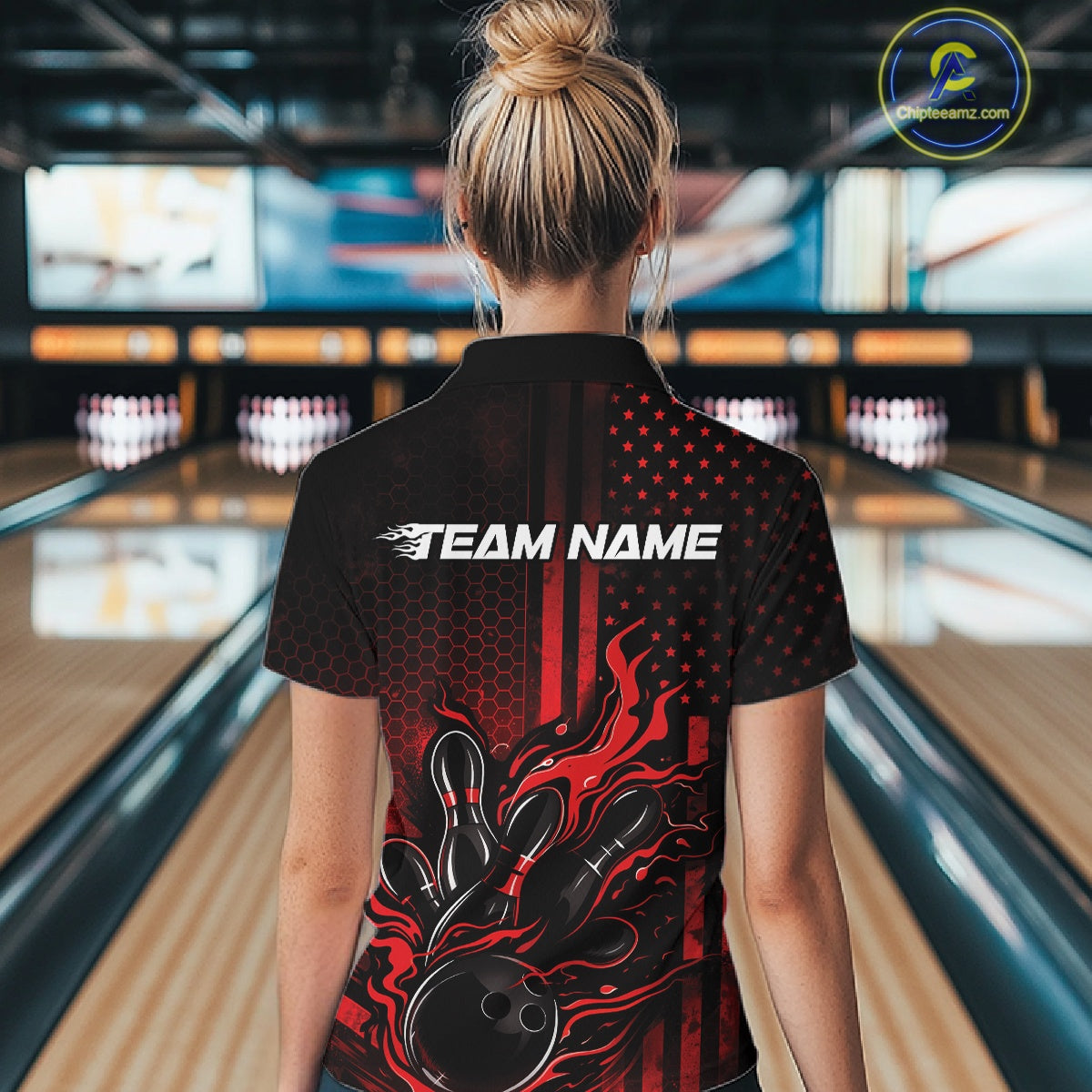 Back view of a female model in a bowling alley wearing a black and red quarter-zip shirt showcasing a flaming bowling ball hitting the pins.