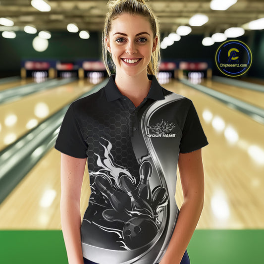 Female model front view in bowling lane wearing black and gray polo shirt with flaming bowling ball striking pins in energetic action scene.