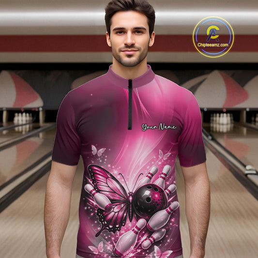 Male model at a bowling lane wearing a pink bowling quarter-zip shirt with butterfly artwork, a bowling ball, and scattered pins.
