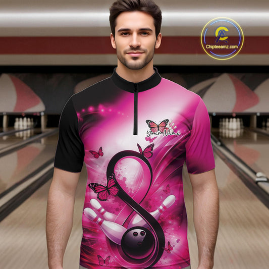 Male model in a bowling alley wearing a quarter-zip shirt with a pink ribbon, bowling ball, and butterfly illustration.