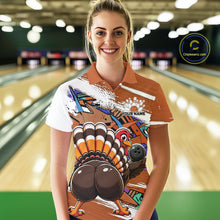 Load image into Gallery viewer, Front view of a female model wearing an orange custom bowling polo shirt with a funny graffiti turkey holding a bowling ball, paint splatter accents, and a personalized name in a bowling alley.
