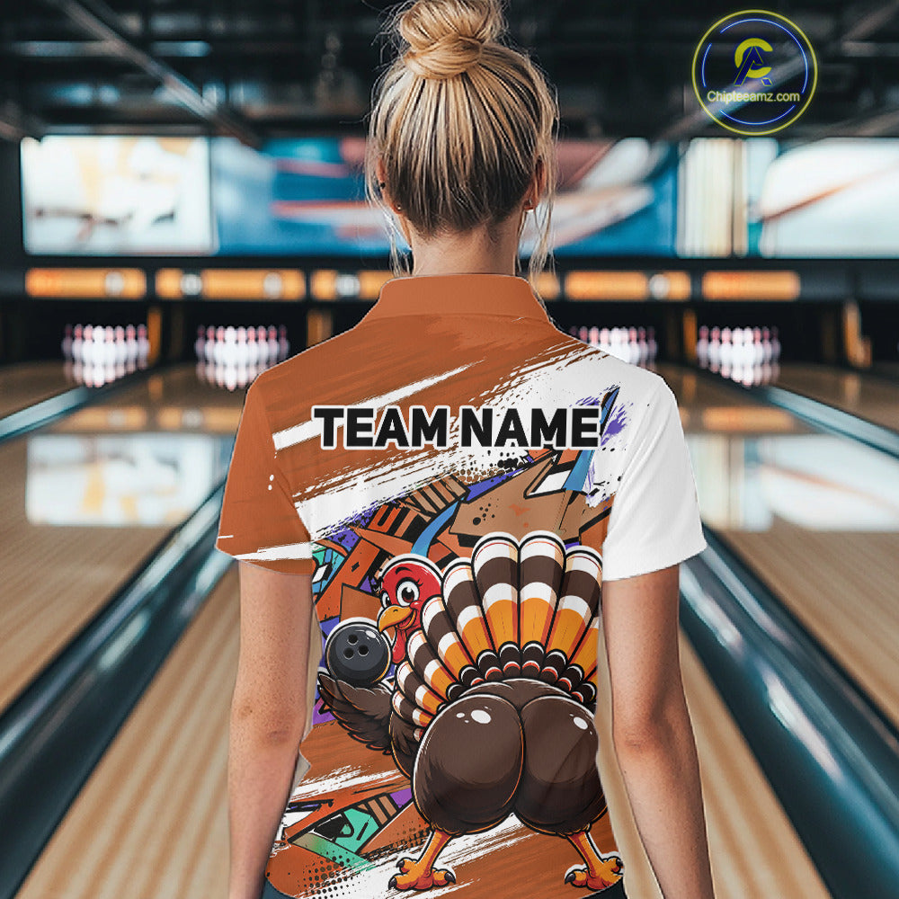 Back view of a female model in a bowling alley wearing an orange custom quarter zip bowling shirt with a funny graffiti turkey holding a bowling ball, paint splatter accents, and a personalized name.