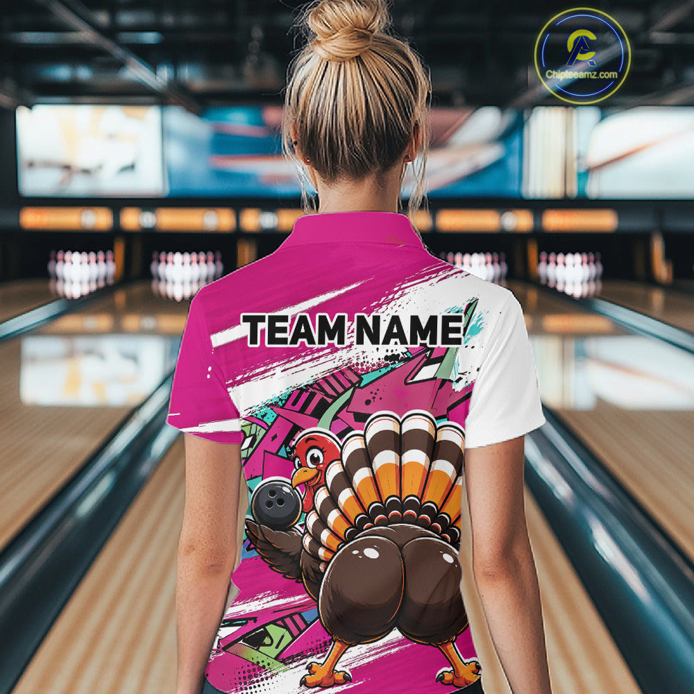 Back view of a female model wearing a pink custom bowling polo shirt with a funny graffiti turkey holding a bowling ball, paint splatter accents, and a personalized name in a bowling alley.