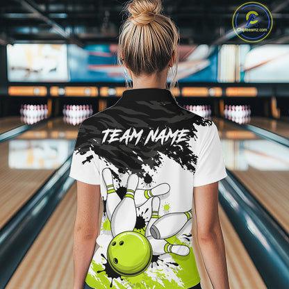 A woman viewed from behind wearing a custom bowling-themed polo shirt in a bowling alley. The back of the white and black polo features a lime green bowling ball graphic, white bowling pins, and the text 'TEAM NAME'.