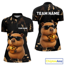Load image into Gallery viewer, Two polo shirts with a capybara design holding a golden ball, one with 'Your Name' and the other with 'Team Name', on a white background.