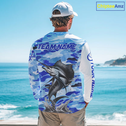 A man wearing a sailfish fishing shirt long sleeve with a large fish graphic and 'TEAM NAME' text, standing by the ocean.