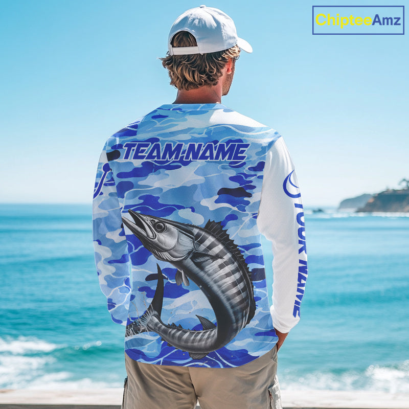 Person wearing a wahoo fishing shirt long sleeve with a wahoo fish design and 'TEAM NAME' text on the back, standing by the ocean.