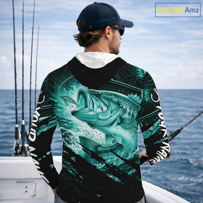 Person wearing a teal and black bass fishing shirt with a fish design, standing by the ocean.