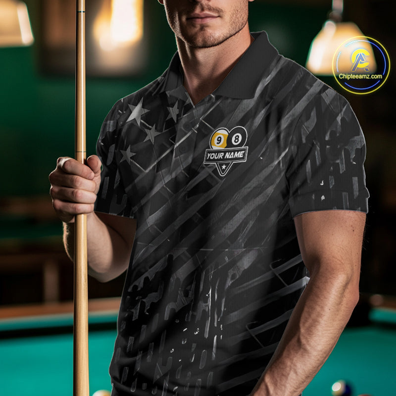 Man wearing a black polo shirt with pool ball design and text, holding a pool cue in a billiards setting.