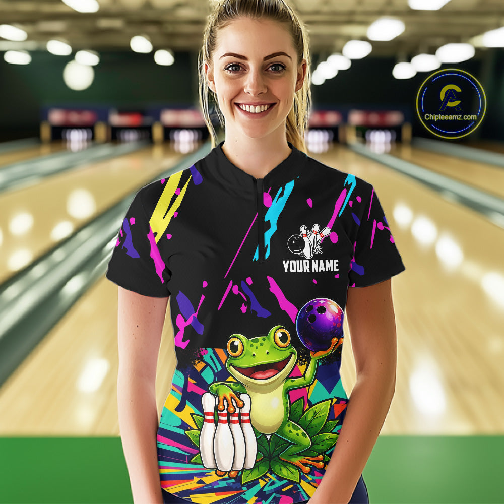 Person wearing a black bowling shirt with colorful design and frog graphic in a bowling alley.