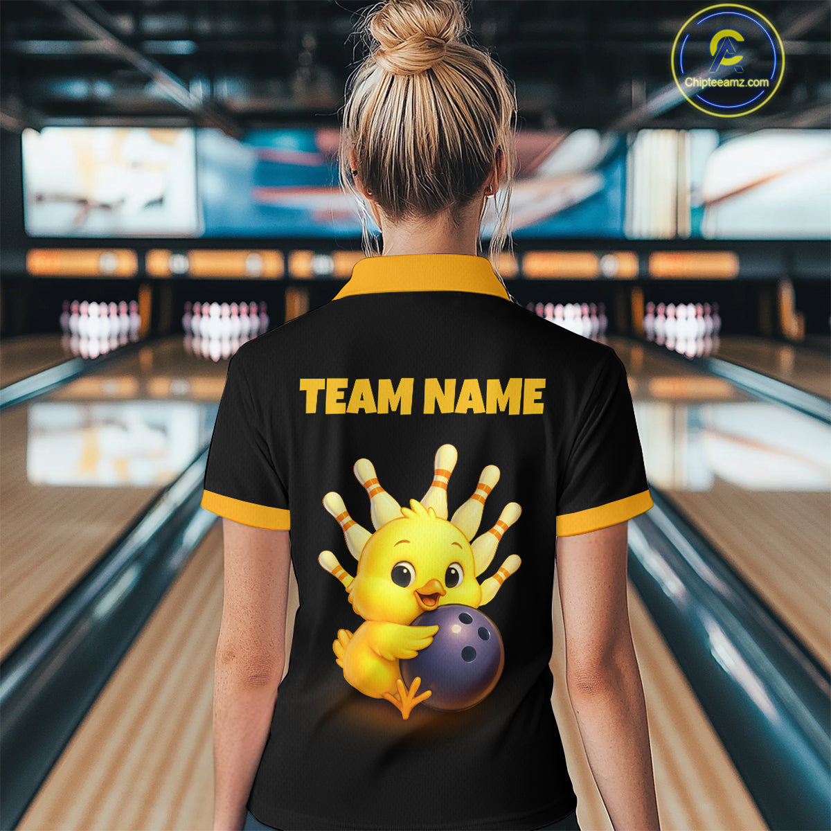 Person wearing a black bowling shirt with a cartoon chicken holding a bowling ball and 'TEAM NAME' text in a bowling alley.